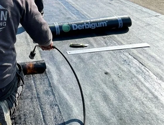 Chalumeau et rouleau de bitume pendant la réparation d'un toit plat à Namur par Grognon Roofing