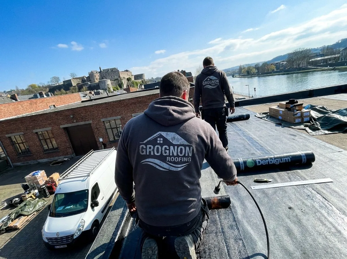 Étancheur de Grognon Roofing soudant un roofing bitume sur le toit plat d'un immeuble de briques à Namur, la Citadelle et la Meuse en face